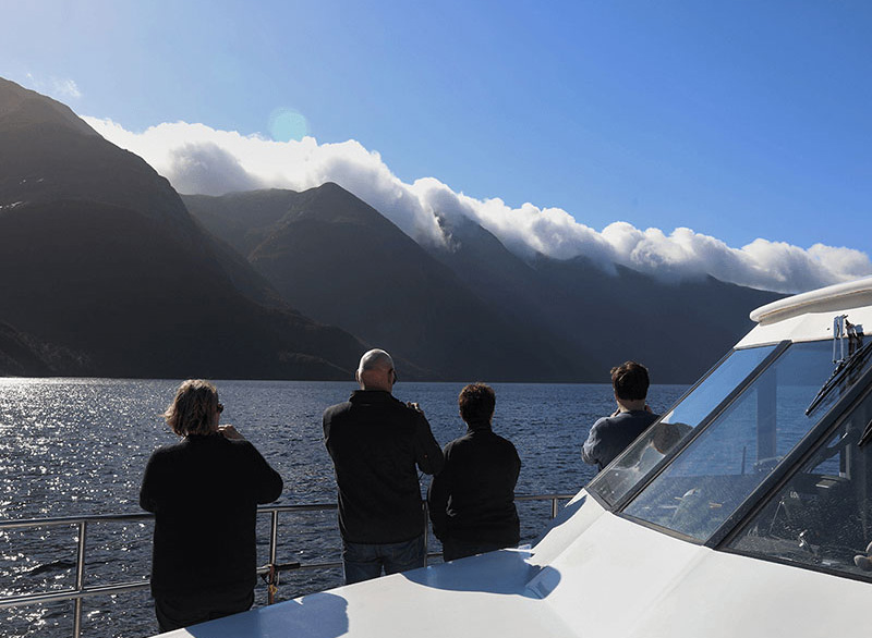 Four passengers onboard the Southern Secret taking photos of the cloud formations above the mountains in the distance.